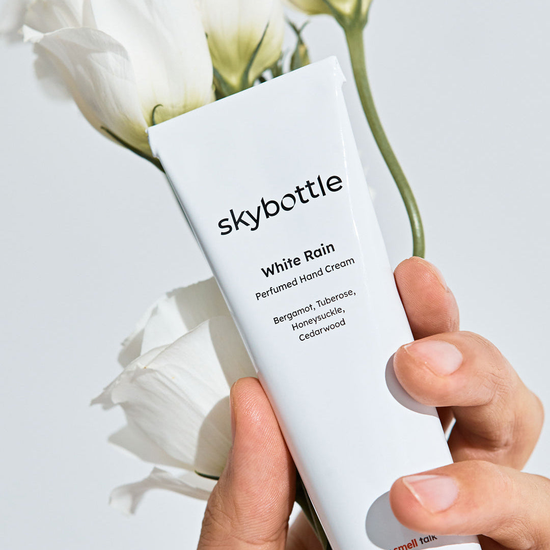 Skybottle Perfumed Hand Cream White Rain 50ml held in hand with flowers